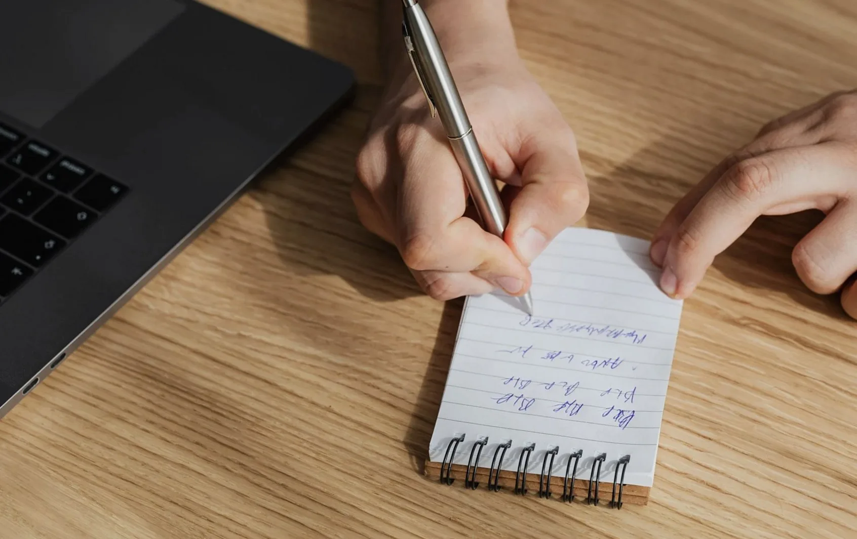 ノートパソコンの横で手書きのメモを取る手元